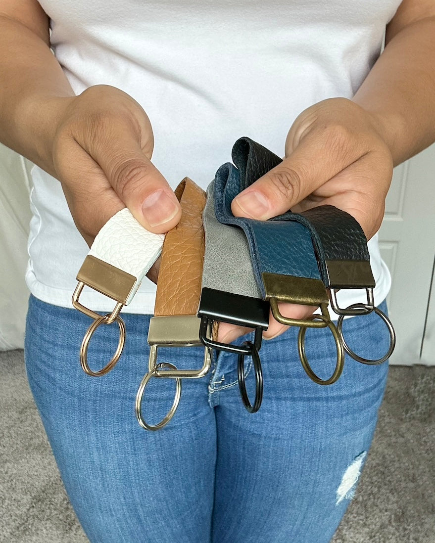 Girl holding Genuine leather ketchain wristlets in multiple colors. Navy blue, black, tan, gray, and white.